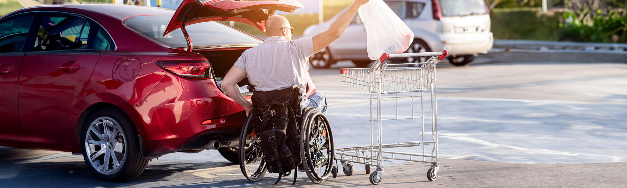 disabled man in a wheelchair puts purchases in the trunk of a car