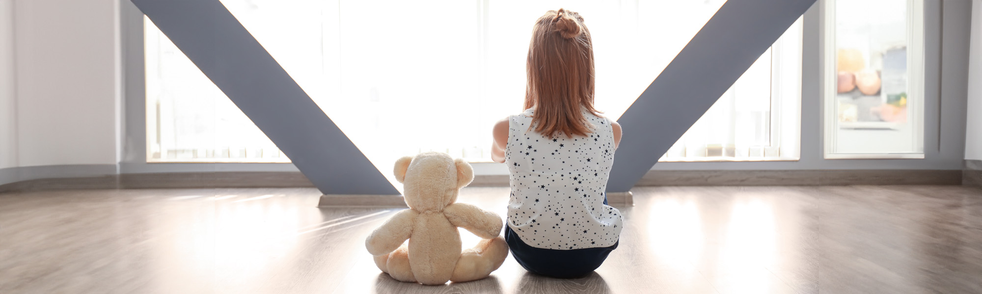 little girl with teddy bear sitting on floor near window