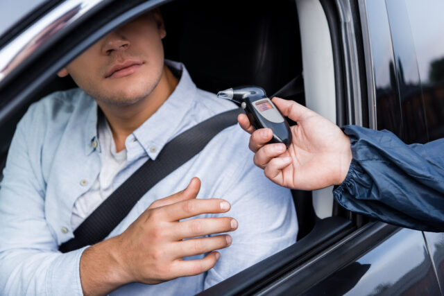 cropped view of driver taking breathalyzer from policeman while sitting in car, stock image