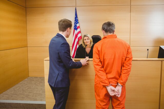 Lawyer and judge speaking next to the criminal in handcuffs