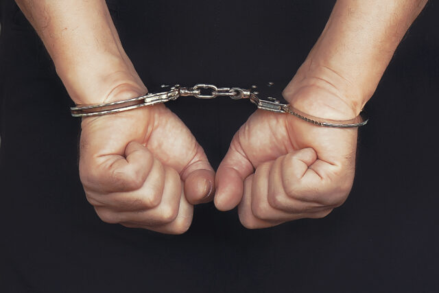 Criminal hands locked in handcuffs. Close-up view