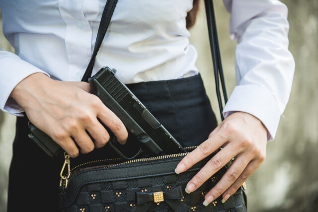 Young woman self defense putting gun in her small handbag