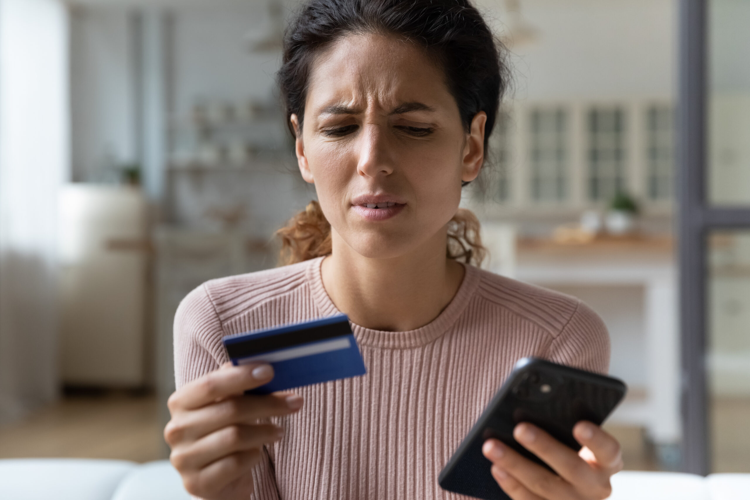Close up of frown Latina woman hold credit card smart phone experiences problems with e-payment, feels annoyed due lack of money, payment insecurity, insufficient funds. Victim of fraud, scam concept
