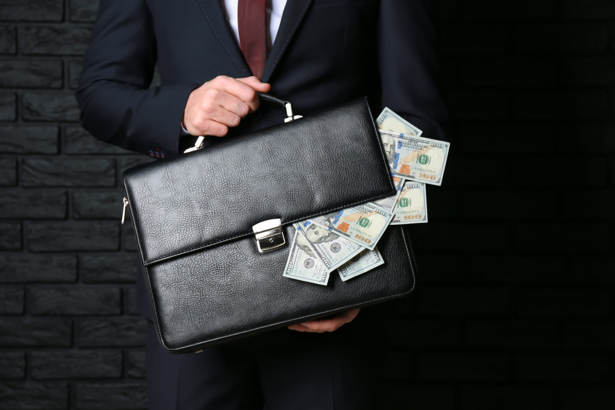 Businessman holding briefcase with dollar banknotes on dark background. Corruption concept