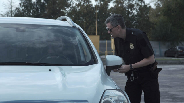 Police officer stopping the driver of a vehicle and questioning him over an alleged offence through the open window of the car